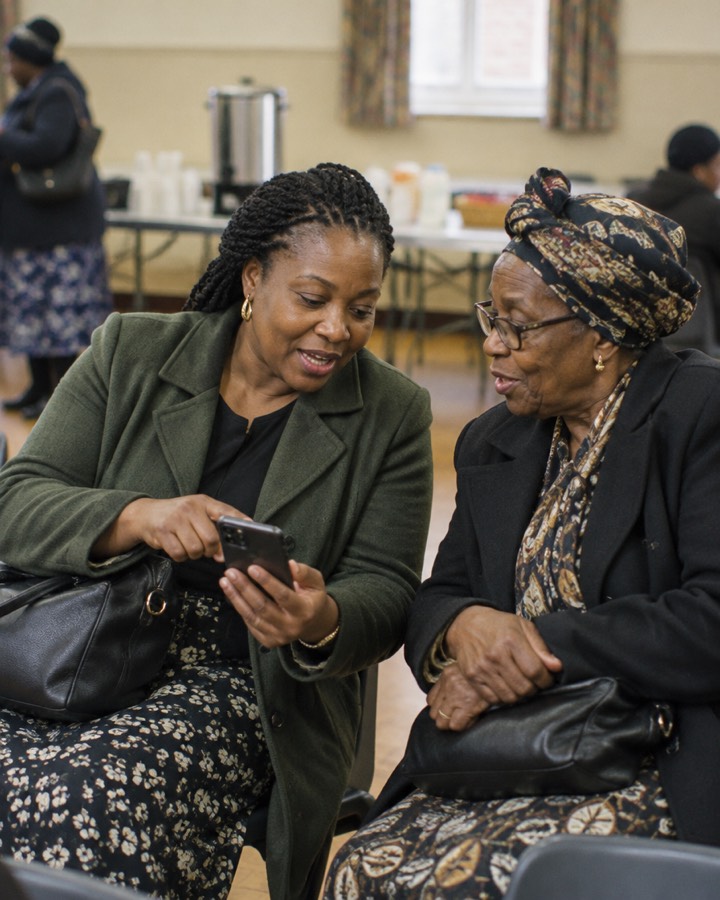 Two women at a community gathering looking at a phone together